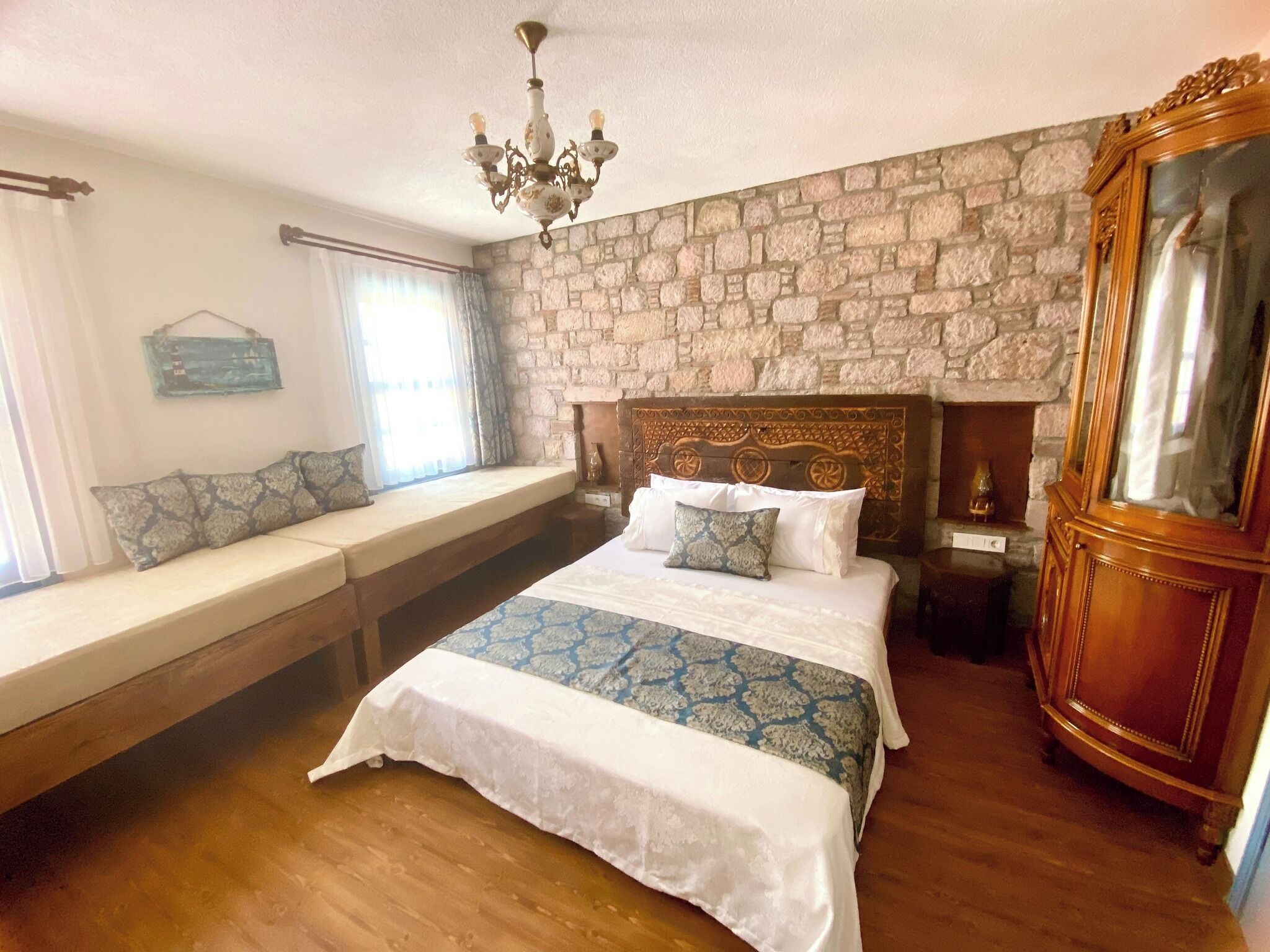 Ein Schlafzimmer mit einer Steinwand, einem großen Bett mit Holz-Kopfteil, einer Bank mit Kissen, einer Kandelaber und einem Holzschrank.