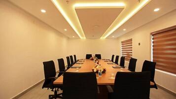 Uma sala de conferência com uma mesa comprida, cadeiras pretas e uma luminária no teto.