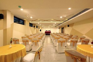 A banquet hall with rows of tables and chairs, a stage at the front, and a modern ceiling design. - Veliyil Castles (Cherthala)