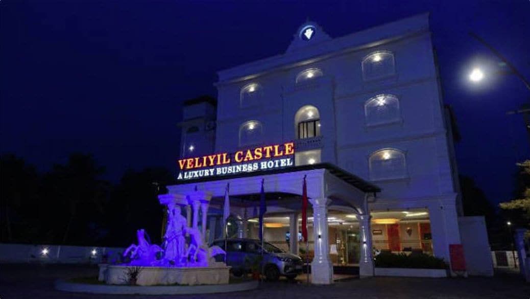 Um edifício com uma placa indicando "Veliyil Castle Luxury Business Hotel" e uma fonte em frente.