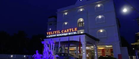 A building with a sign reading "Veliyil Castle Luxury Business Hotel" and a fountain in front.