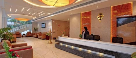A hotel reception area with a marble floor, a reception desk, and a staircase leading to an upper level.