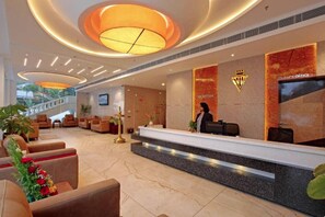 Uma área de recepção de hotel com piso de mármore, um balcão de atendimento e uma escadaria que leva a um andar superior.
