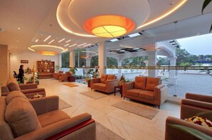 A spacious lobby with comfortable seating, a reception desk, and large windows offering a view of the outdoors. - Veliyil Castles (Cherthala)