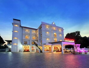 Um hotel com vários andares, uma entrada marcante e uma escadaria que leva aos pisos superiores, com uma placa indicando "VELIYIL CASTLE".