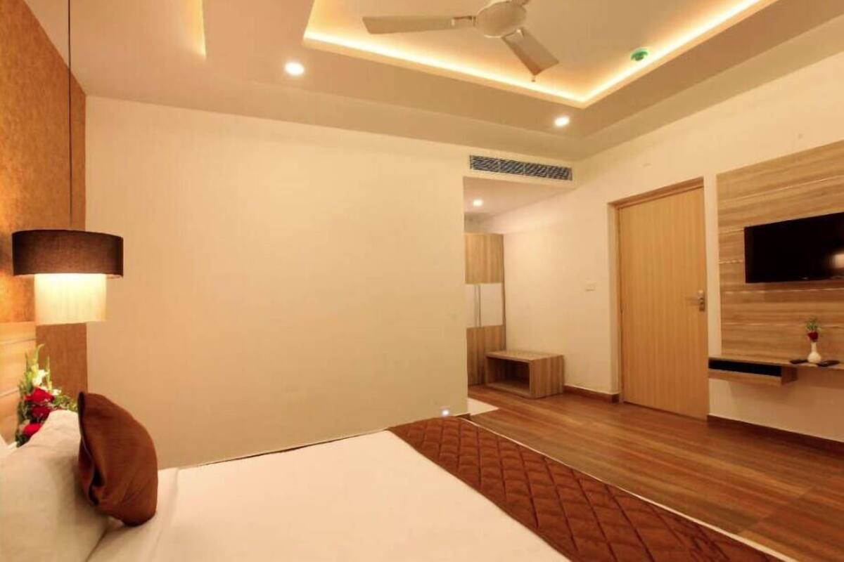 A modern hotel room with a bed, a ceiling fan, a TV, and a wooden floor.