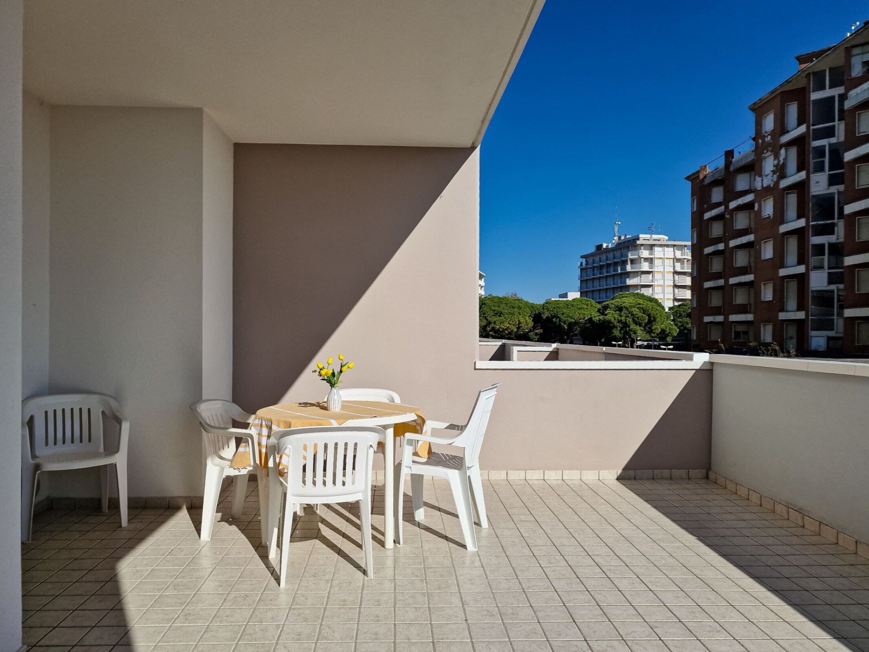 Un balcone con tavolo e sedie, un vaso con fiori gialli e vista su edifici sullo sfondo.
