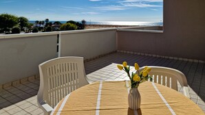 Ein Balkon mit Tisch und Stühlen, eine Vase mit gelben Blumen und Blick aufs Meer.
