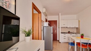 Eine kompakte Küche mit weißen Schränken, einem Kühlschrank, einer Mikrowelle und einem Essbereich mit Tisch und Stühlen.