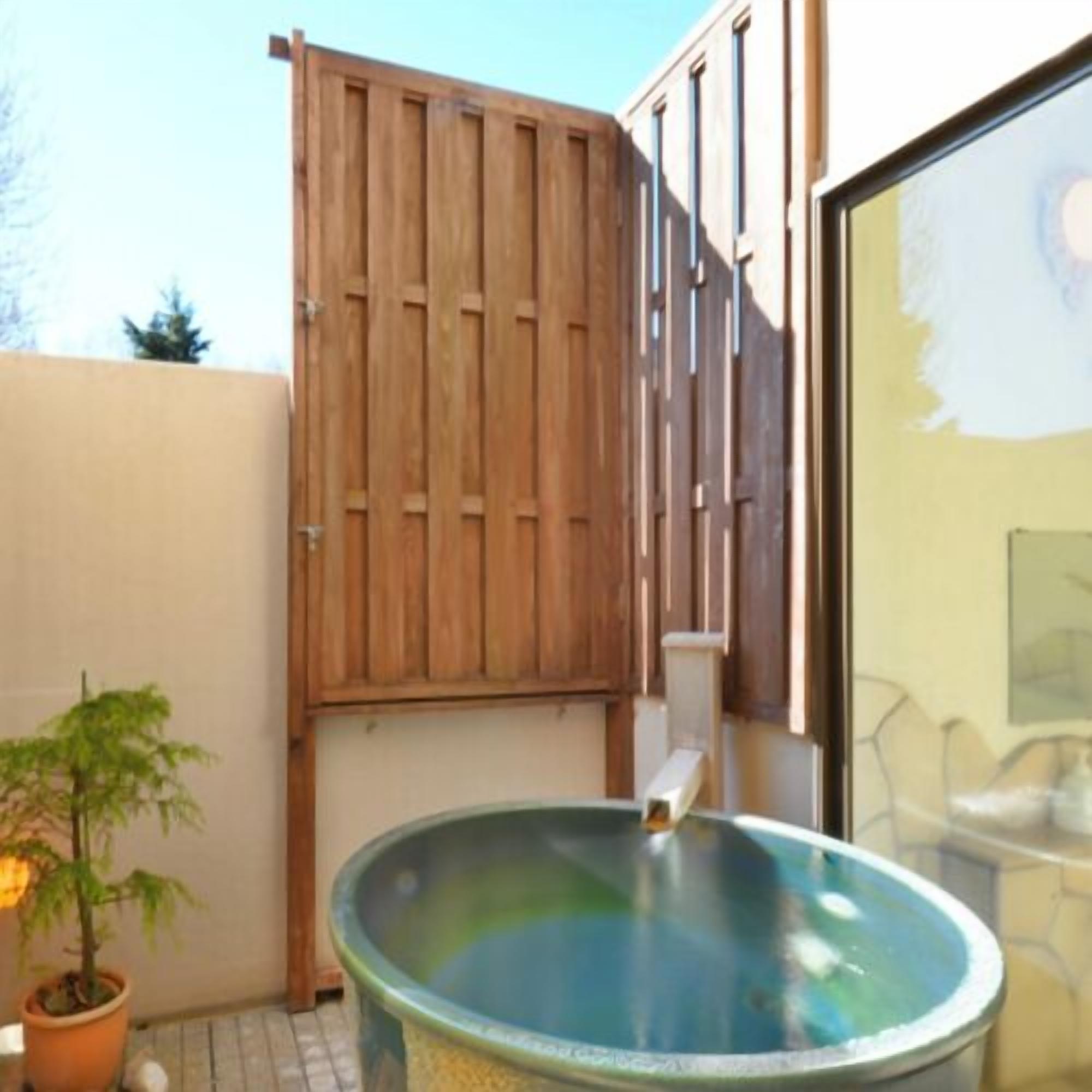 A hot tub in a covered outdoor area with a wooden fence and a potted plant.