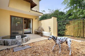 Un chien se promène dans une cour où se trouvent un jacuzzi en pierre, un banc en bois et une zone délimitée par une clôture.