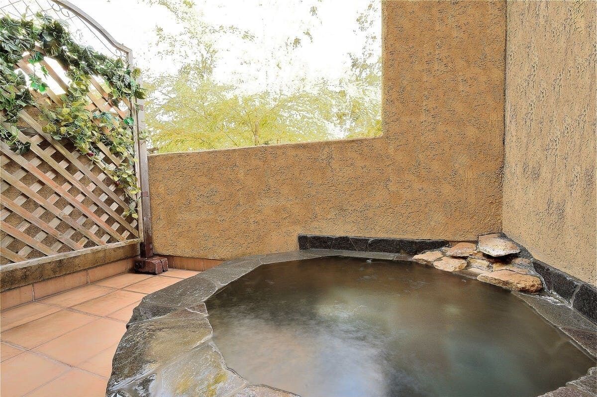 A hot tub area with a stone basin, surrounded by a wooden fence and a textured wall.
