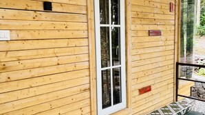 Una cabaña de madera con un ventanal grande, un porche con tejas y una pequeña zona de estar al aire libre.