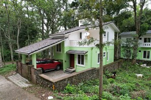 A two-story house with a car parked in front, surrounded by greenery.