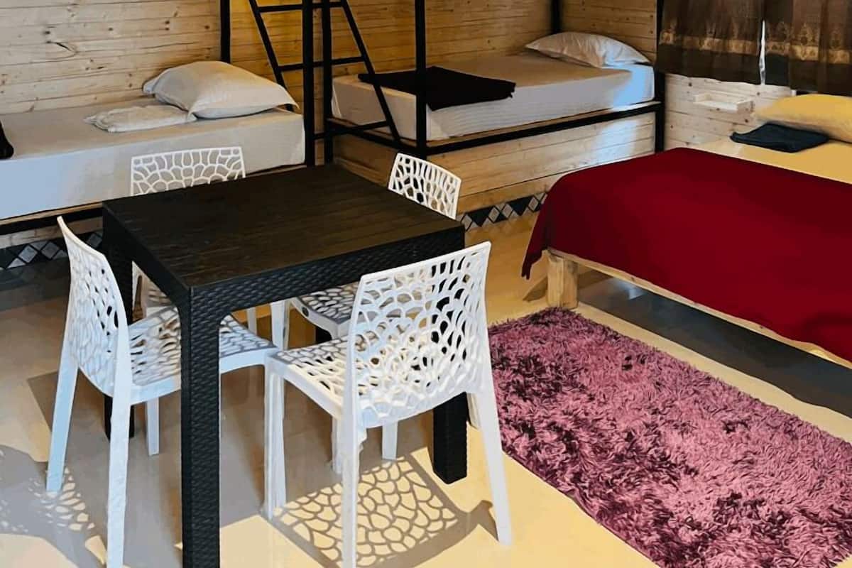 A compact room with bunk beds, a dining table with chairs, and a ceiling fan.