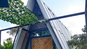 Una estructura triangular con una puerta de madera, rodeada de follaje y vigas de metal.