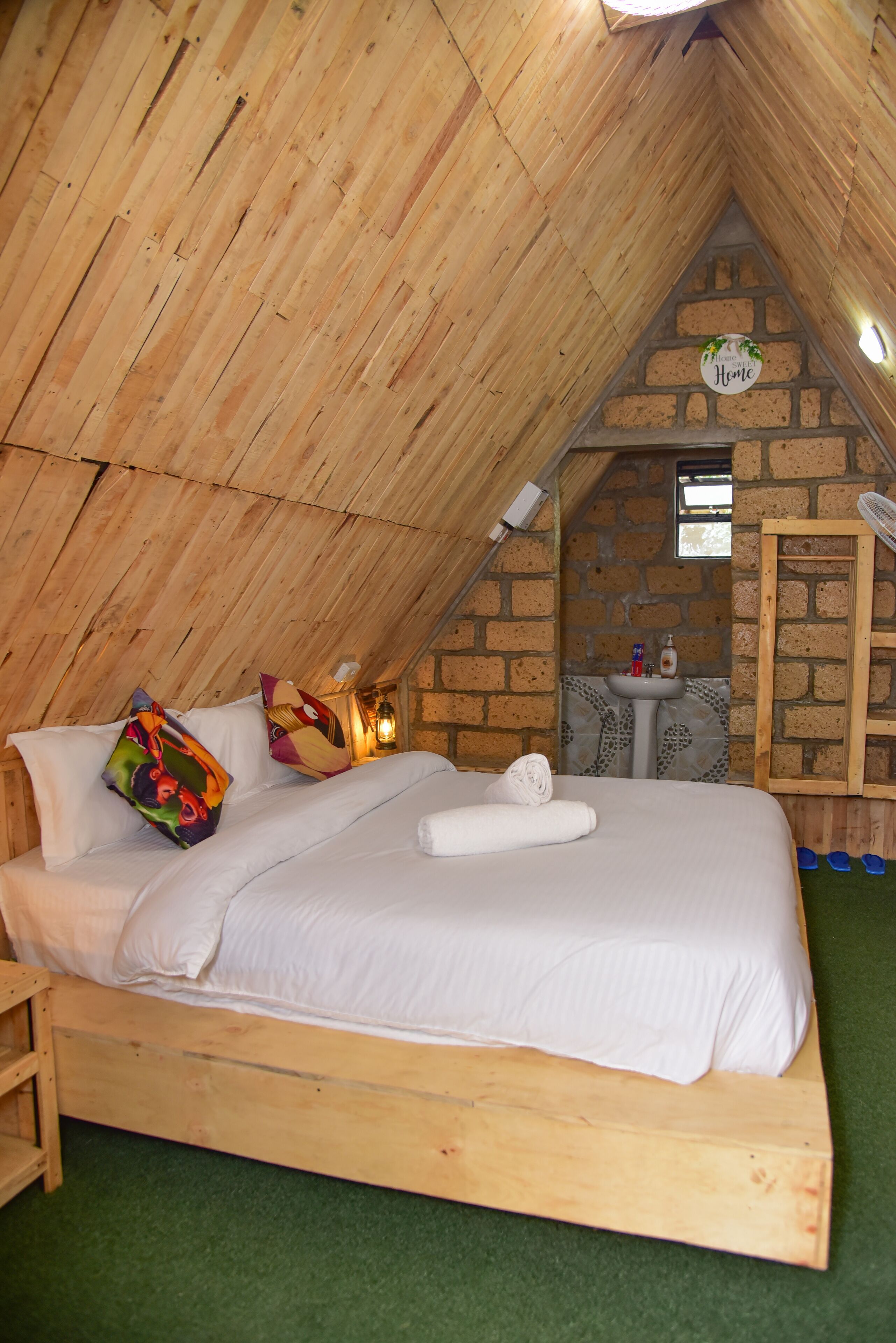 Un dormitorio acogedor en el ático con una cama de madera, almohadas coloridas, un lavamanos pequeño y una pared de piedra.