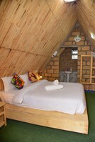 Un dormitorio acogedor en el ático con una cama de madera, almohadas coloridas, un lavamanos pequeño y una pared de piedra.