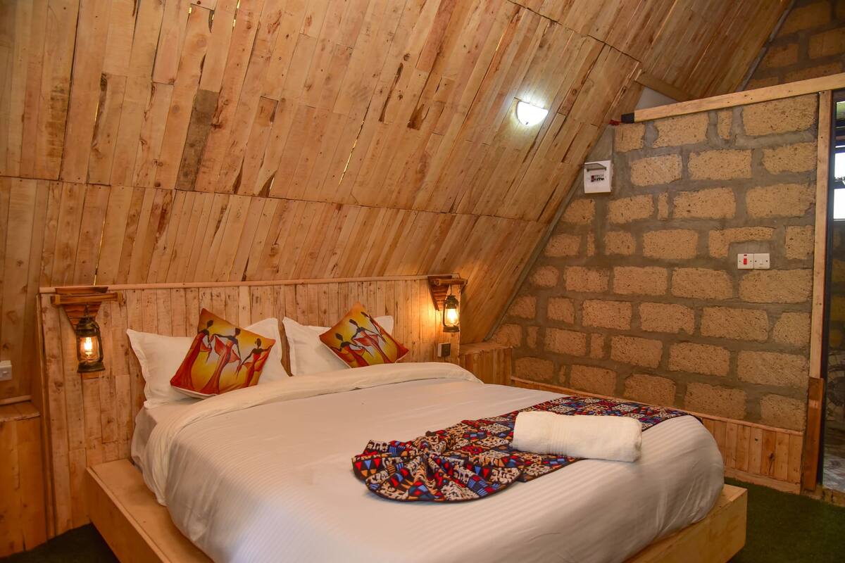 A wooden-paneled room with a bed, a stone wall, and a wooden ceiling.