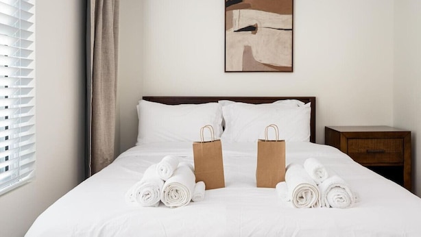 Ein Hotelzimmer mit einem ordentlich bezogenen Bett, zwei braunen Papiertüten und gerollten Handtüchern auf dem Bett.