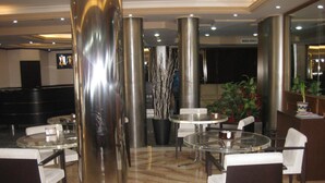 A modern lobby with round glass tables and white chairs, large metallic columns, and a reception desk with a potted plant. - Hotel Florida (Albacete)
