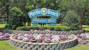 Un letrero da la bienvenida a visitantes a Myrtle Beach con un jardín paisajístico al frente.