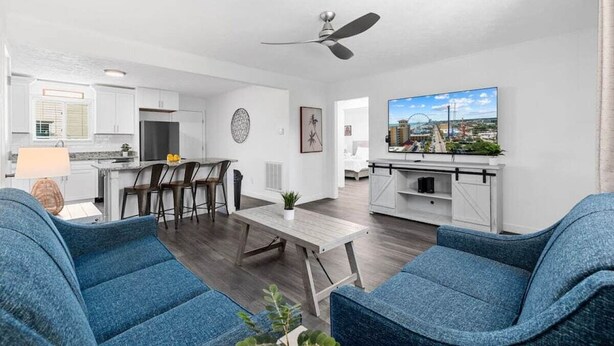 Una sala de estar moderna con comedor, cocina y un televisor mostrando un paisaje urbano.