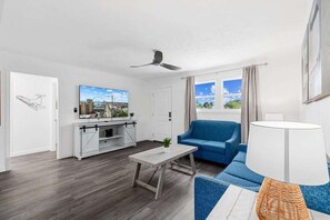 Ein modernes Wohnzimmer mit einem blauen Sofa, einem Holztisch, einem Fernseher und einem Deckenventilator.
