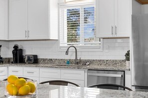 Eine moderne Küche mit weißen Schränken, einer Granitabdeckung, einer Edelstahl-Spüle und einem Fenster mit Jalousien.