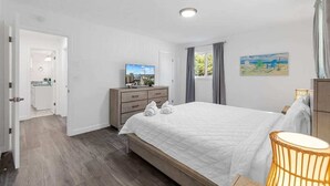 Un dormitorio con cama, cómoda, televisor y un cuadro en la pared.