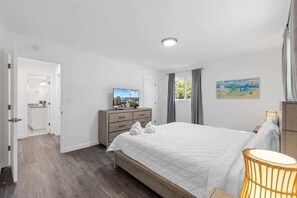 A bedroom with a bed, a dresser, a television, and a painting on the wall.