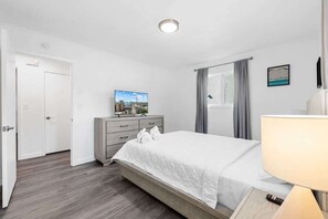 Ein Hotelzimmer mit Bett, Fernseher auf einer Kommode, einem Fenster mit Vorhängen und einer Tür.