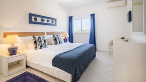 A bedroom with a bed, nightstand, lamp, and a view of the city through the window. - Prainha Family Holidays (Portimão)