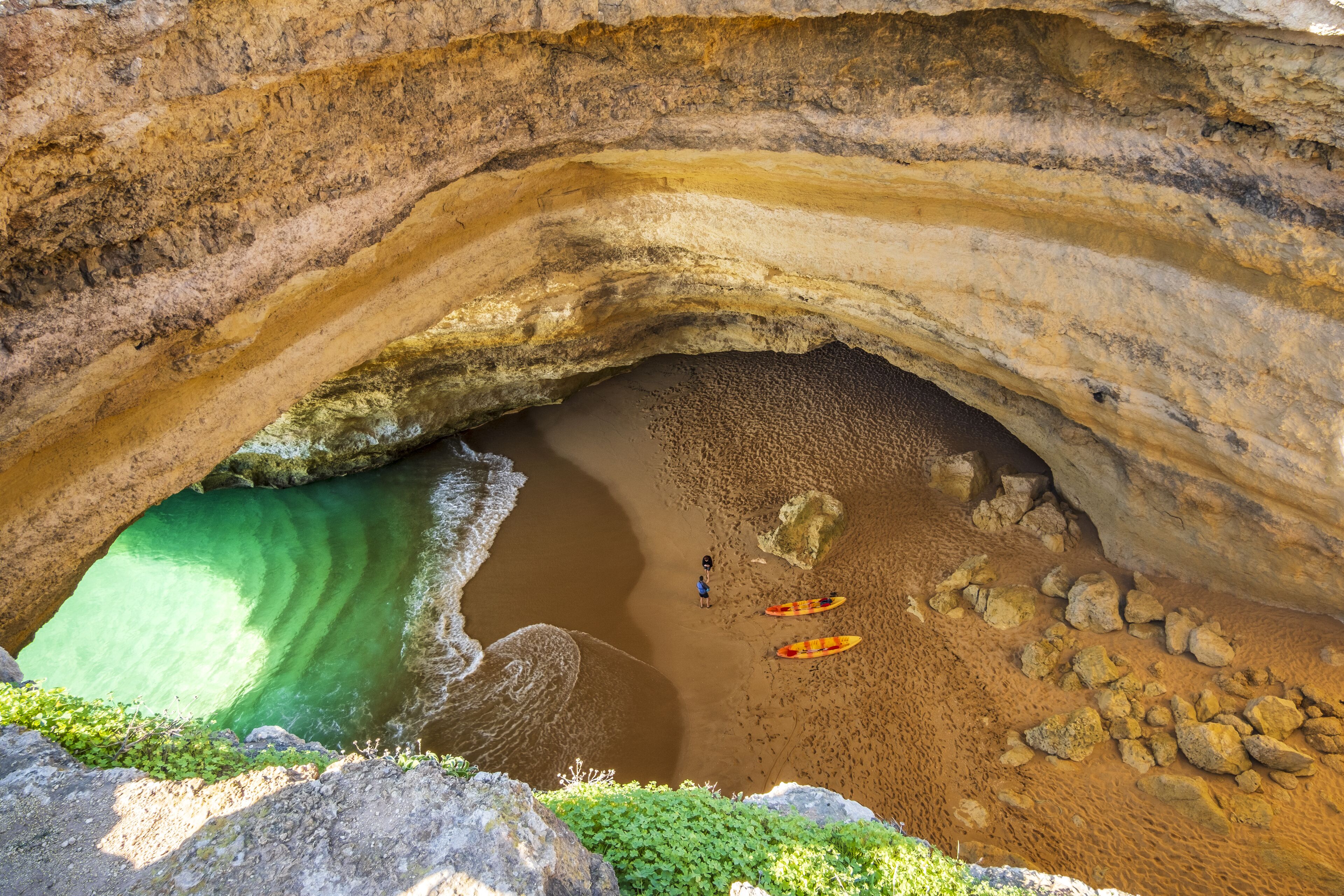 A natural cave with a sandy beach and a green pool.