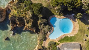 An aerial view of a coastal property with a swimming pool, rocky cliffs, and lush greenery. - Prainha Family Holidays (Portimão)