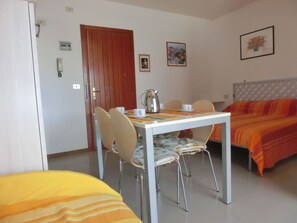 Een kamer met een bed, een tafel met stoelen, een waterkoker en een lijst met een afbeelding aan de muur.