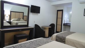 Habitación de hotel con un espejo grande, una mesita redonda pequeña, dos sillones negros y una cama con colcha estampada en gris y blanco.