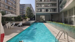 En pool med en metallstege, omgiven av en kakelbeklädd poolterrass och vita solstolar.