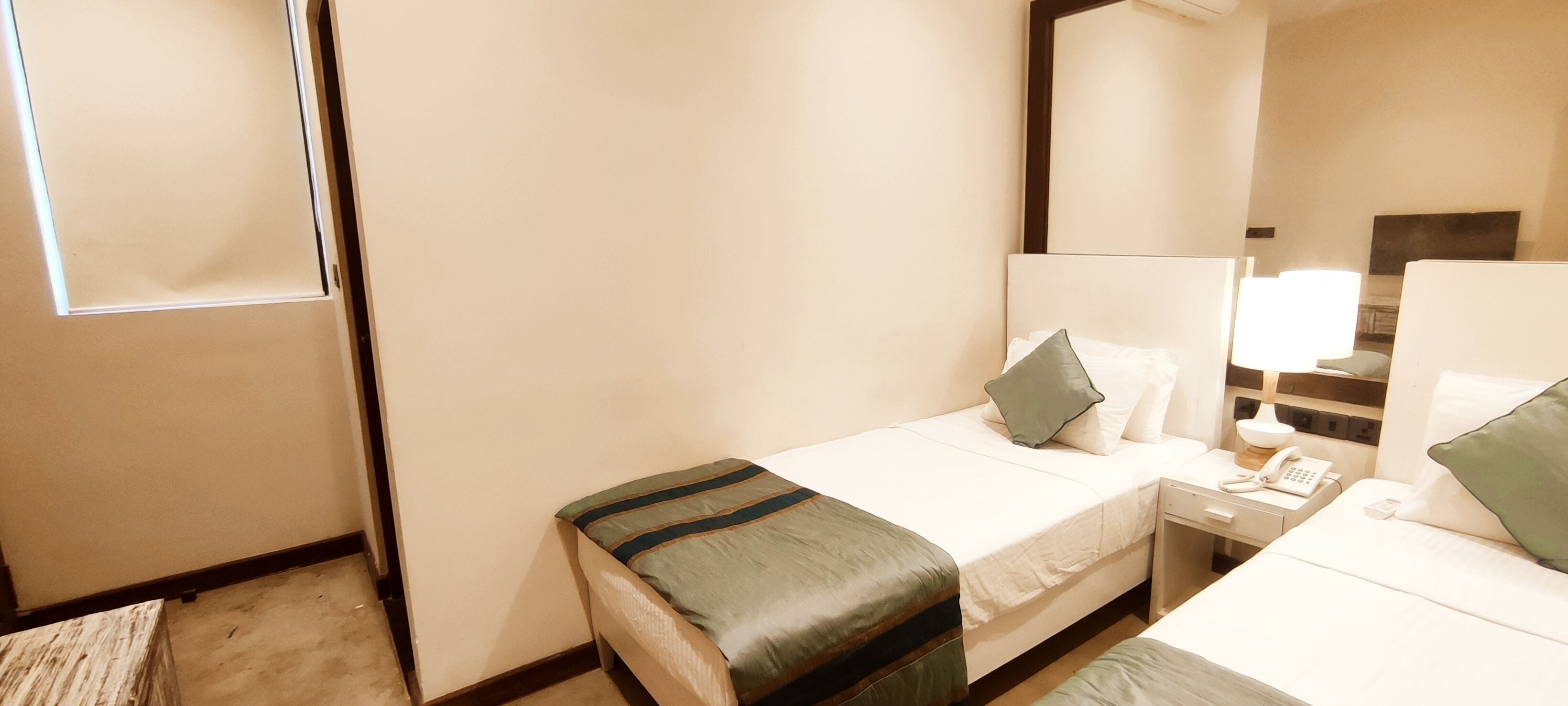Una habitación de hotel con dos camas individuales, una mesita de noche con lámpara, un teléfono y un espejo.