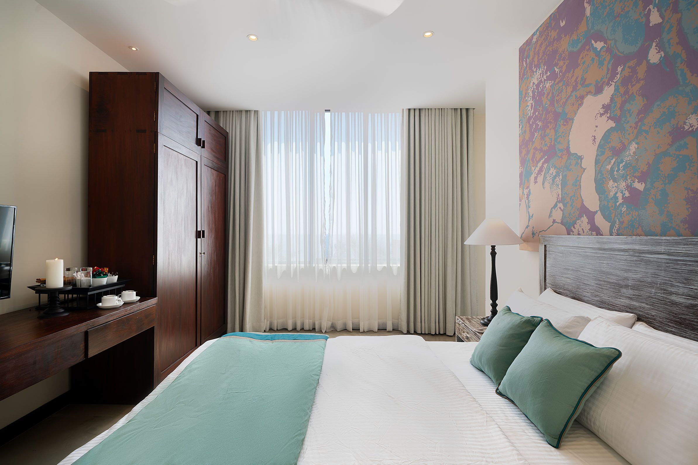 A hotel room with a large bed, a desk with a lamp, a TV, and a painting on the wall.