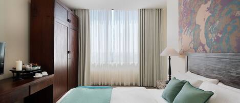 A hotel room with a large bed, a desk with a lamp, a TV, and a painting on the wall.