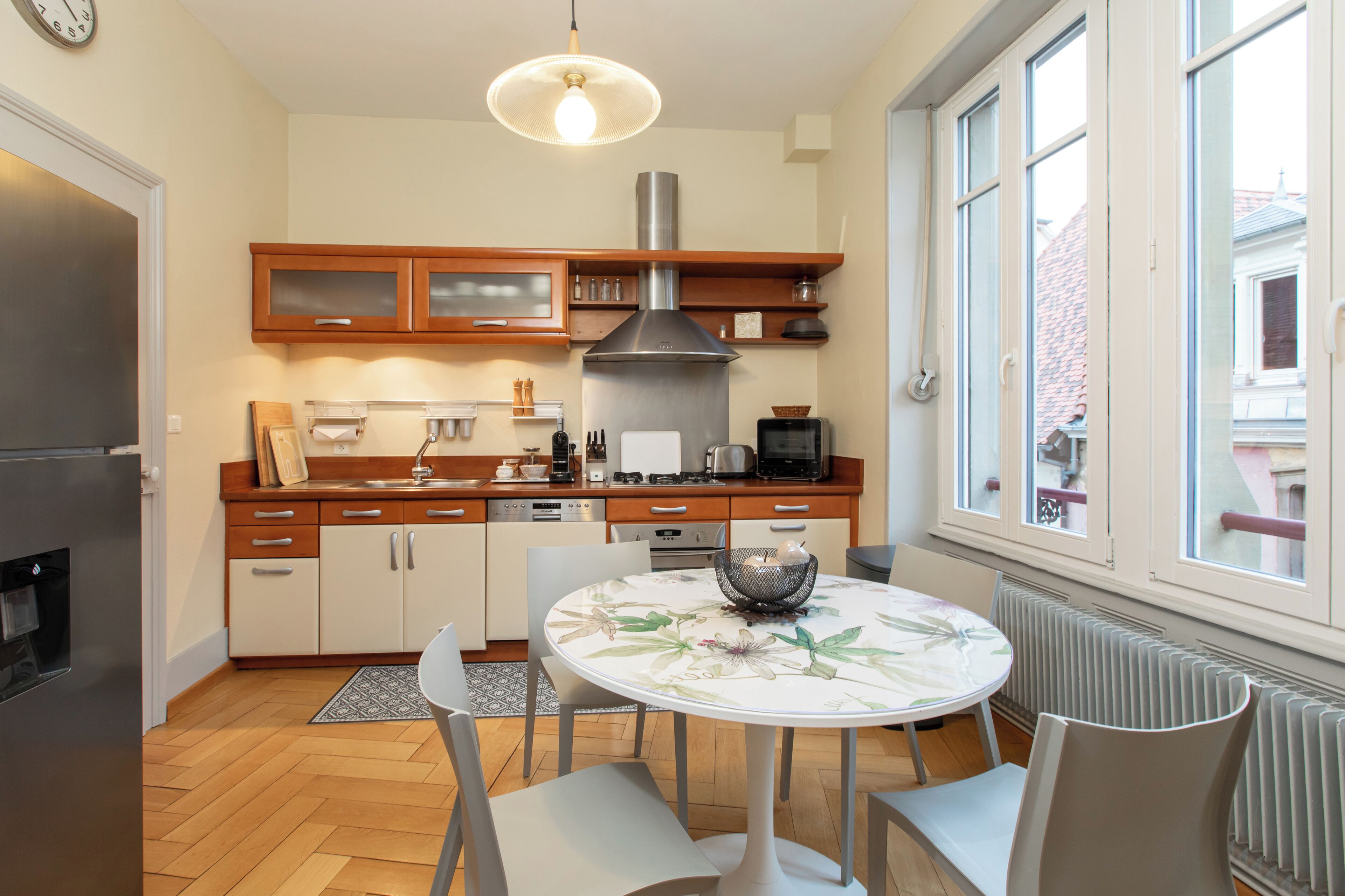A modern kitchen with wooden cabinets, a stainless steel range hood, and a dining area with a round table and chairs.