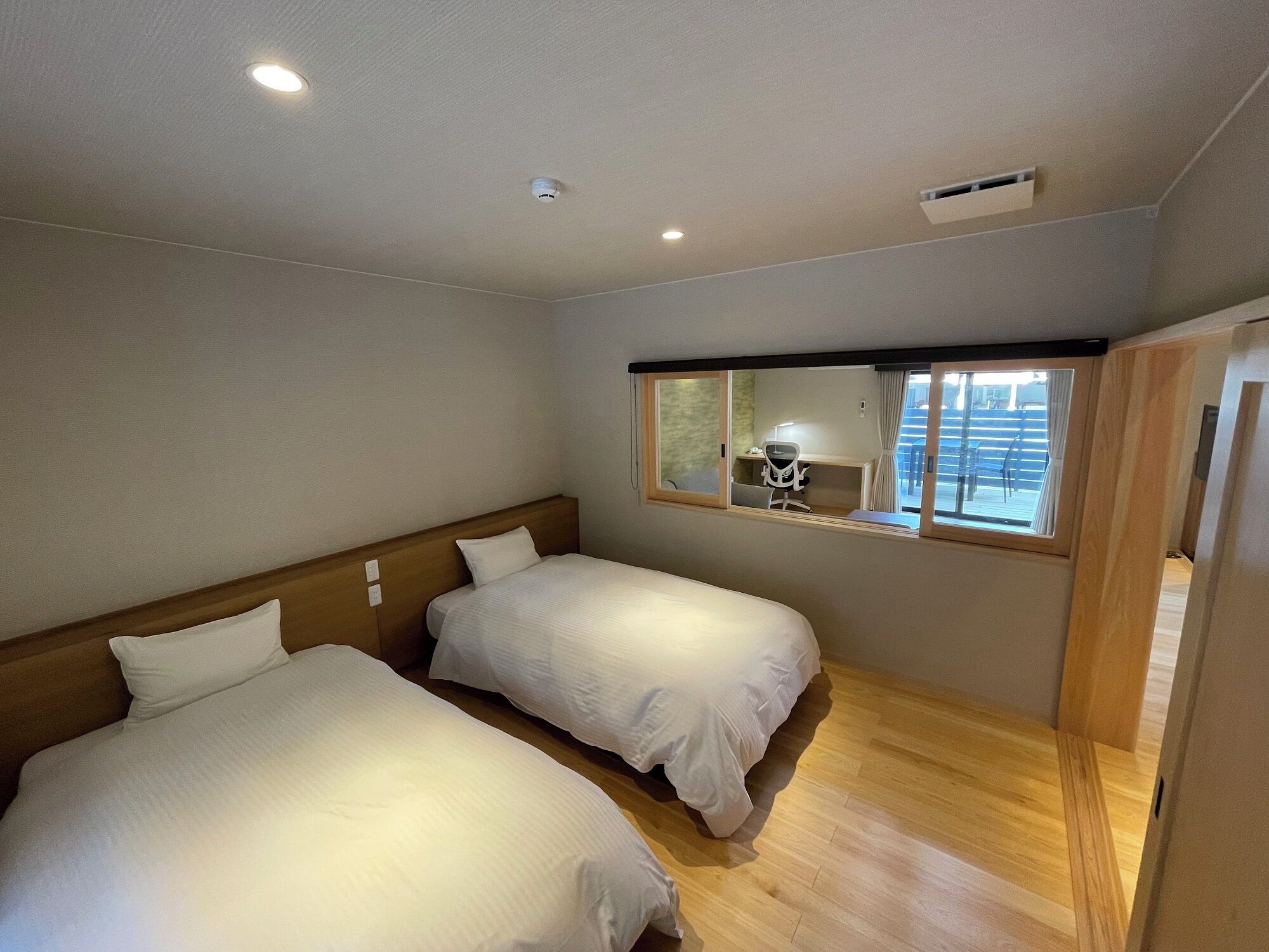 Une chambre d’hôtel avec deux lits, des têtes de lit en bois, une grande fenêtre donnant sur un beau paysage et un bureau avec une chaise.