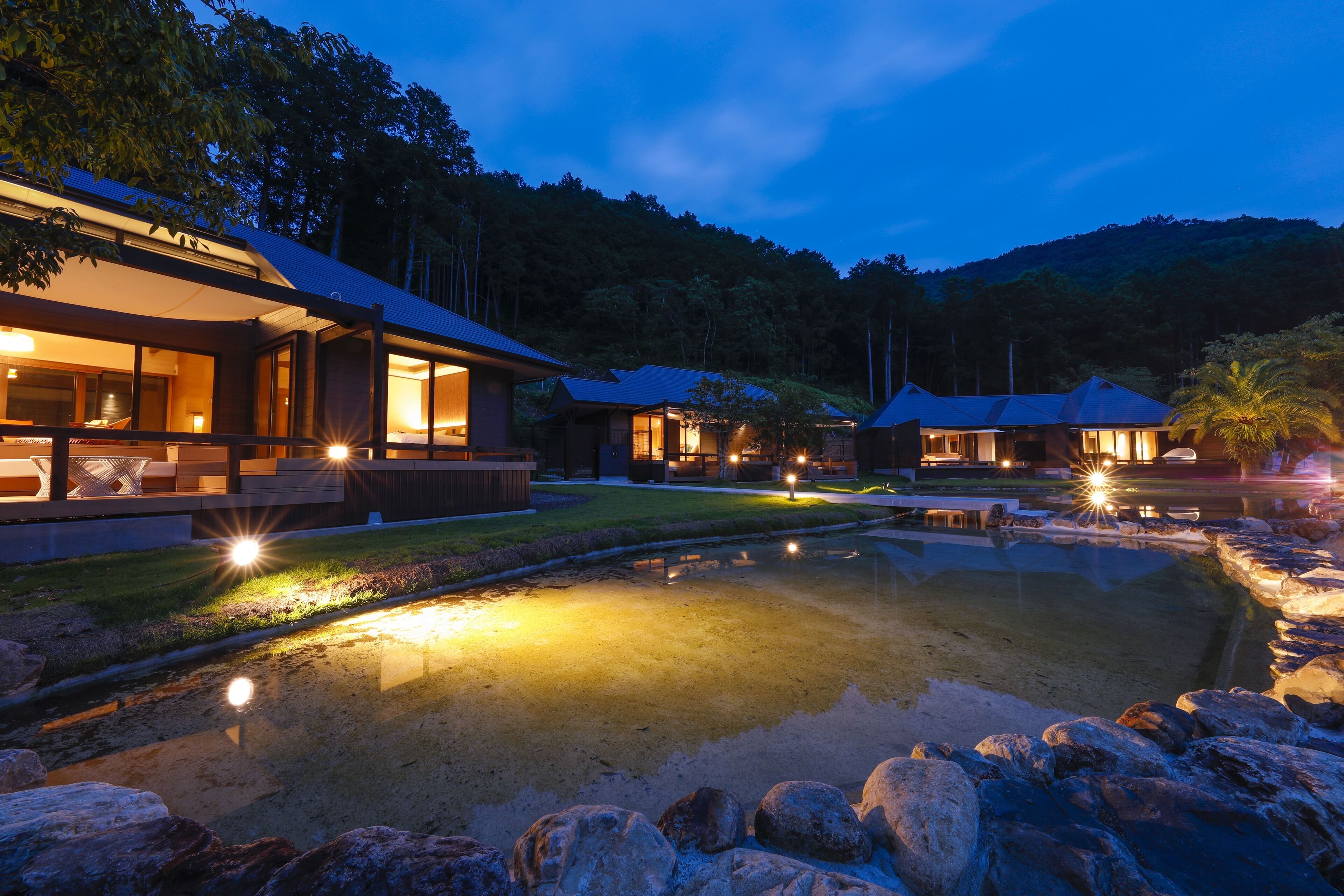 A modern resort with a large pool, well-lit outdoor areas, and multiple buildings with large windows.