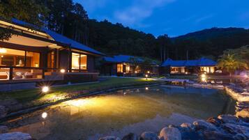 A modern resort with a large pool, well-lit outdoor areas, and multiple buildings with large windows.