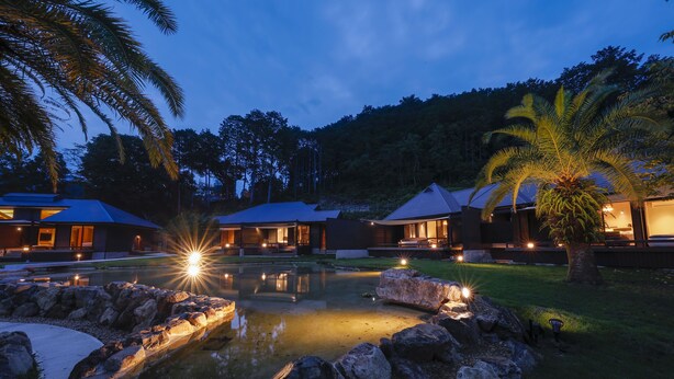 A resort with multiple buildings, a swimming pool, and a well-lit garden area at dusk. - Villa Otogibanashi (Kihoku)