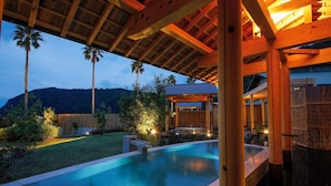 A swimming pool with a wooden deck and a covered seating area, surrounded by palm trees and a mountain backdrop. - Villa Otogibanashi (Kihoku)