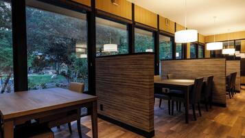 A modern dining area with wooden panel partitions, large windows offering a view of a garden, and pendant lighting.