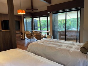 Een slaapkamer met een groot bed, een eettafel met stoelen en een balkon met uitzicht op groen.