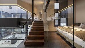 A modern interior with a staircase leading to a bedroom. The room features glass walls, a large bed, and a minimalist design. - Meikeikyo Hanazono (Kutchan)